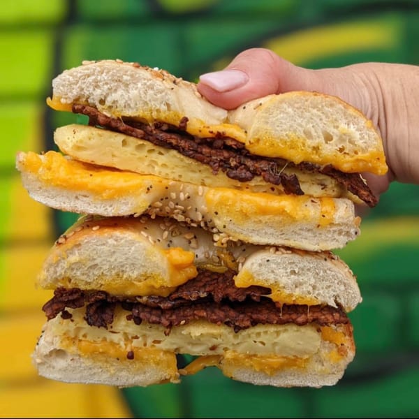 Hand holding a Stella Blue Bistro breakfast bagel sandwich with egg, cheese, and sausage.