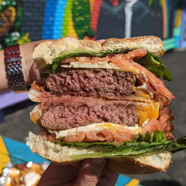 A Stella Blue Bistro breakfast burger, cut in half, revealing two patties, egg, bacon, lettuce, and tomato.