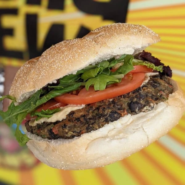 A Stella Blue Bistro black bean burger with lettuce, tomato, and sauce on a bun.