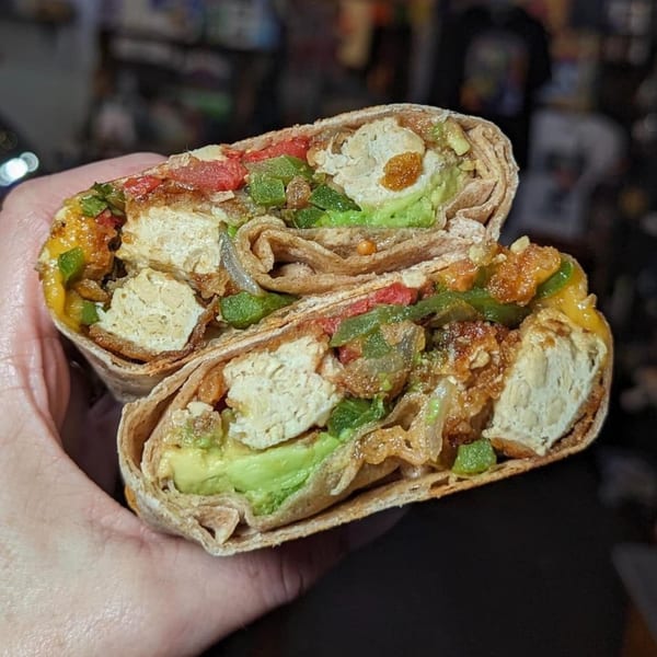 A Stella Blue Bistro breakfast burrito, cut in half, revealing avocado, tofu, and peppers.