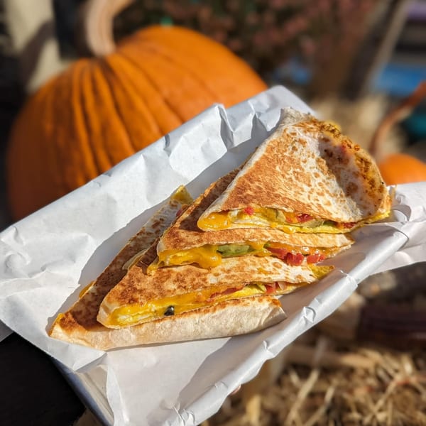 Breakfast quesadillas with melted cheese and vegetables, served in a white paper-lined basket with pumpkins in the background.