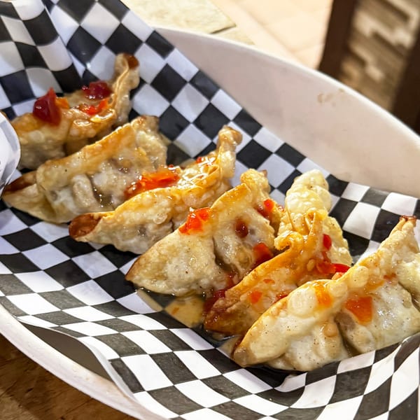 Fried dumplings with sweet chili sauce in a black and white checkered paper liner.