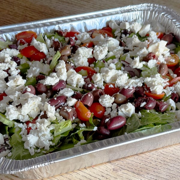 A large catering tray of Greek salad with lettuce, tomatoes, olives, and feta cheese.